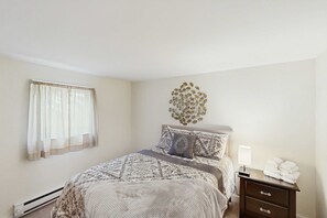 A bedroom with a bed, a bedside table with a lamp, a wall decoration, and a window with curtains. - Cozy 3BR Condo- Indoor Pool- Near Ski & Waterpark (Tannersville)