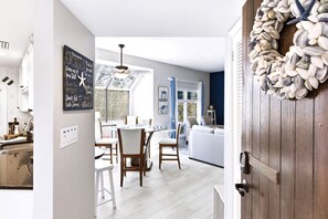 A modern kitchen with white cabinetry, a dining area with a round table and chairs, and a living room with a sofa and a decorative shell wall. - Lagoon-View Villa - Walk to Shelter Cove (Hilton Head Island)