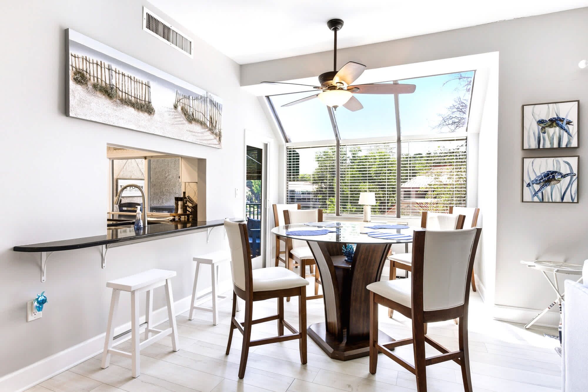 A modern dining area with a round table, white chairs, and a ceiling fan.