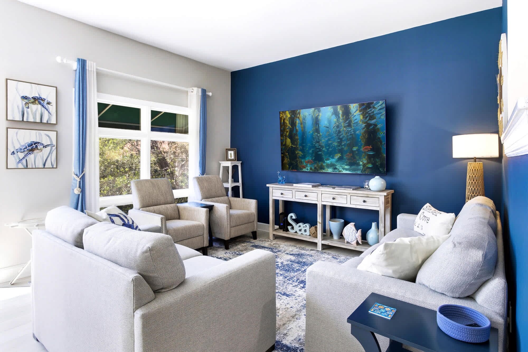 Un salon avec un mur d’accent bleu, un grand tableau et une vue sur l’extérieur.