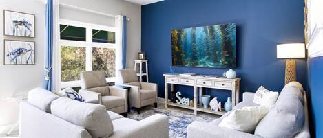 A living room with a blue accent wall, a large painting, and a view of the outdoors.