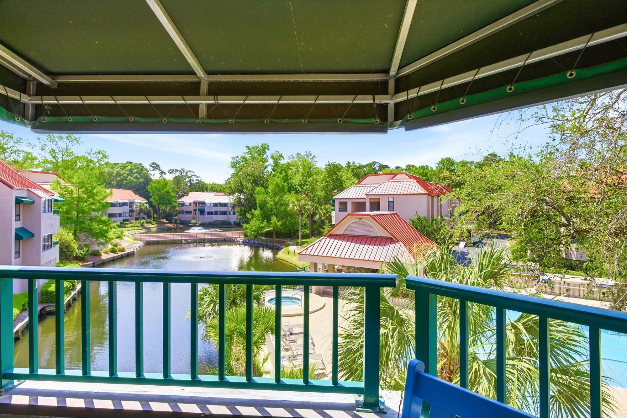A balcony with a view of a river, buildings, and a pool area.