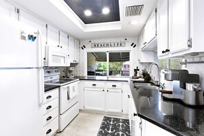 A modern kitchen with white cabinetry, a black countertop, and a sign that reads 'BEACH LIFE'. - Lagoon-View Villa - Walk to Shelter Cove (Hilton Head Island)