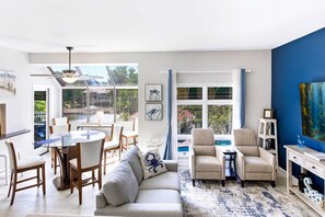 A modern living room with a dining area, large windows, and a view of the outdoors. - Lagoon-View Villa - Walk to Shelter Cove (Hilton Head Island)