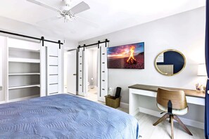 Une chambre à coucher comprenant un lit, un bureau, une chaise, une armoire, un ventilateur de plafond et un téléviseur fixé au mur.