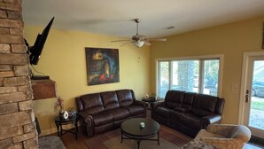Ein Wohnzimmer mit Kamin aus Stein, Ledersofas, einem Couchtisch und einem Deckenventilator.