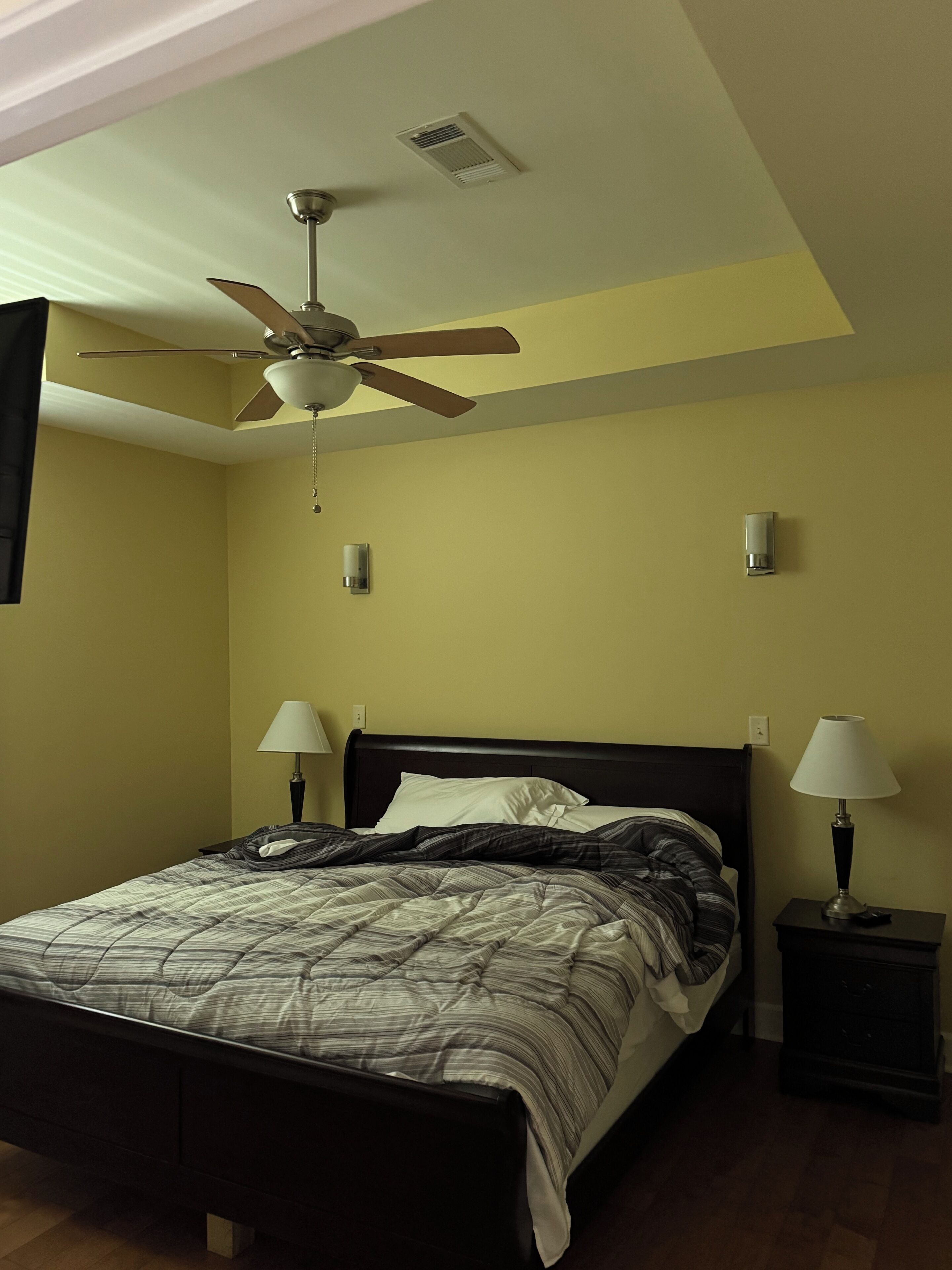 A bedroom with a bed, two bedside lamps, a ceiling fan, and a wall-mounted light fixture.
