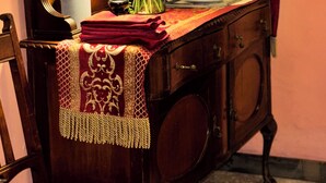 Une pièce comprenant un meuble en bois, une chaise, une table recouverte d’une nappe rouge, une lampe et un tableau accroché au mur.