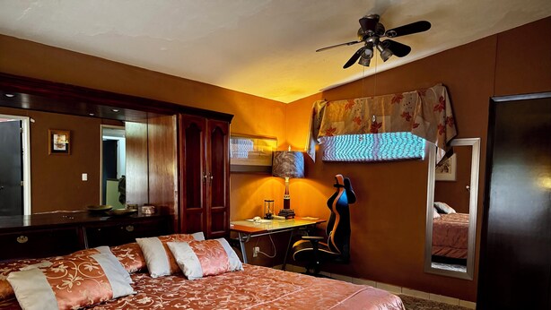 Une chambre d’hôtel avec un grand lit, un bureau avec une lampe, un ventilateur de plafond et un miroir.