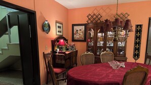 Une salle à manger avec une table ronde recouverte d’une nappe rouge, entourée de chaises en bois dotées d’assises rembourrées.