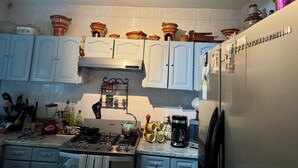 Une cuisine avec des meubles blancs, une cuisinière à gaz, une machine à café et un réfrigérateur.