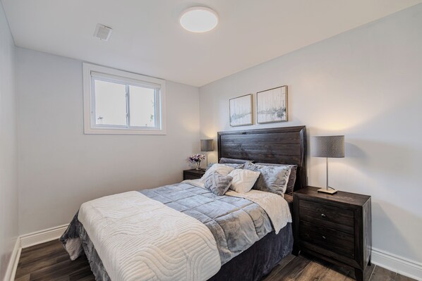 A bedroom with a bed, a nightstand, a lamp, a window, and two wall-mounted pictures.