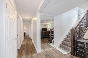 A hallway with wooden flooring, white walls, and a staircase with a wooden handrail.