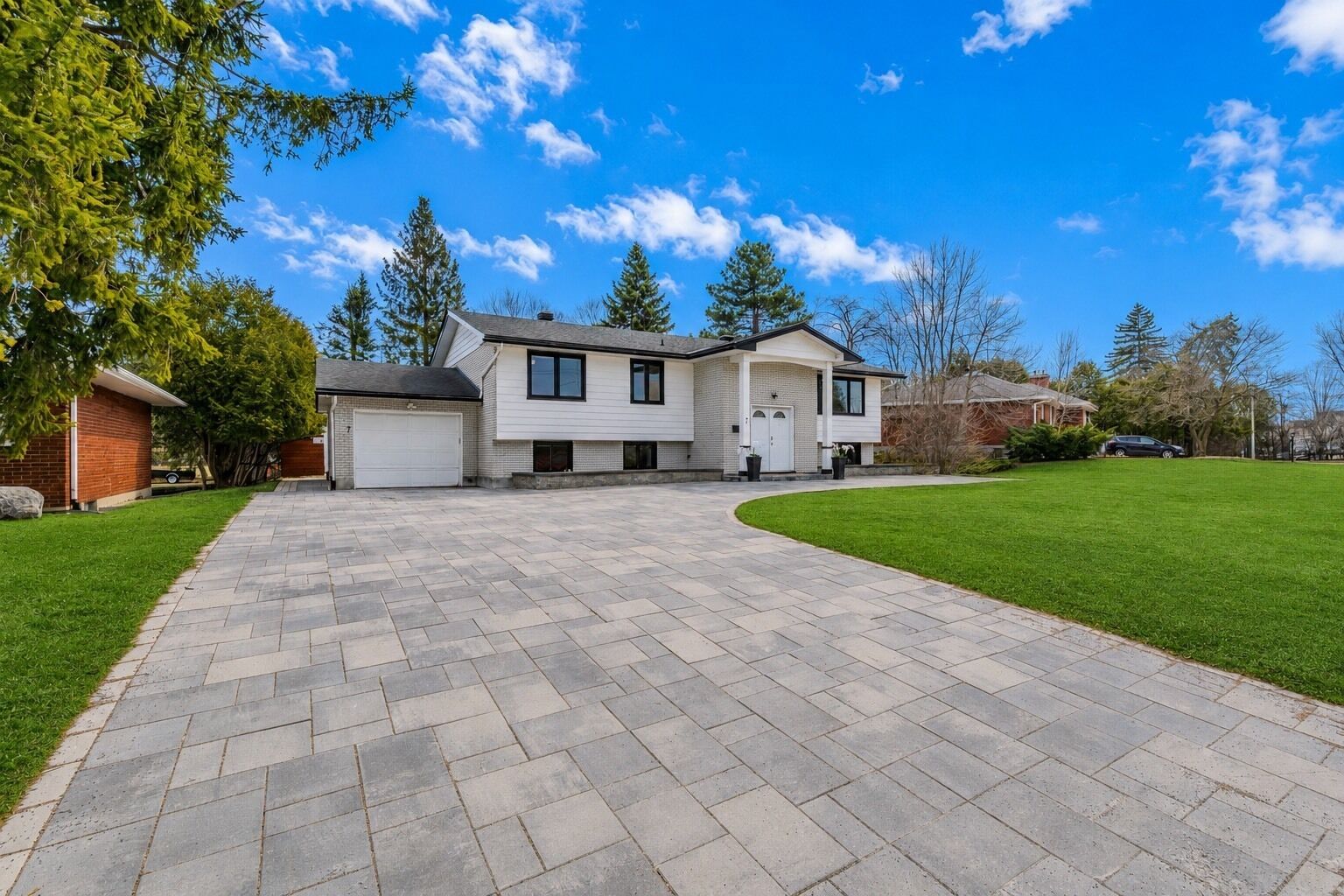 A two-story house with a driveway leading to a garage, surrounded by a well-maintained lawn and trees.