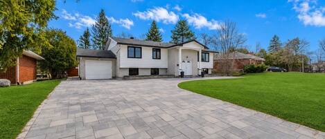 A two-story house with a driveway leading to a garage, surrounded by a well-maintained lawn and trees.
