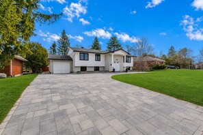 A two-story house with a driveway leading to a garage, surrounded by a well-maintained lawn and trees.