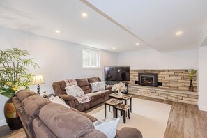 Ein Wohnzimmer mit einer Couch, einem Fernseher, einem Kamin und einem großen Fenster.
