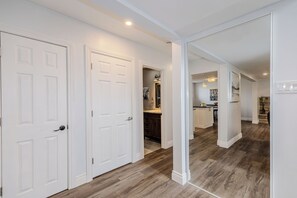 A hallway with white doors, wooden flooring, and a kitchen area visible in the background.
