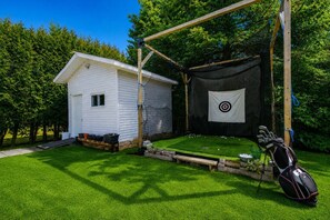 A backyard with a white house, a target on a net, and a golf bag.