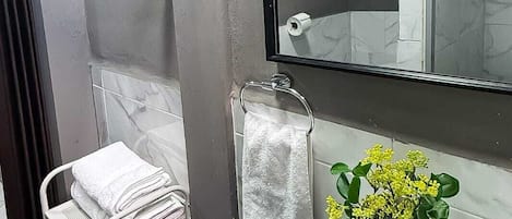 Un baño con un lavamanos blanco, un espejo, un perchero para toallas y una pequeña planta en maceta.