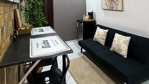 A modern living space with a dining area, a black sofa, a clock, and a ceiling fan.