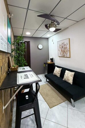 A modern living space with a dining area, a black sofa, a clock, and a ceiling fan.