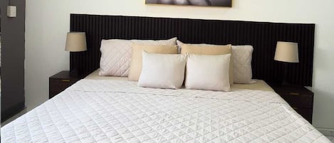 A bedroom with a large bed, two bedside tables, a ceiling fan, and a wall-mounted artwork.
