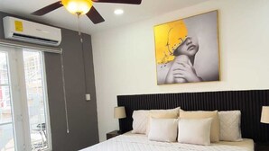 A bedroom with a bed, a ceiling fan, a painting, and a window.
