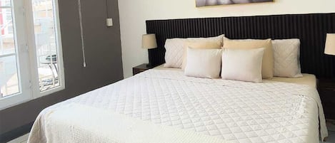 Um quarto com cama, ventilador de teto, pintura e janela.