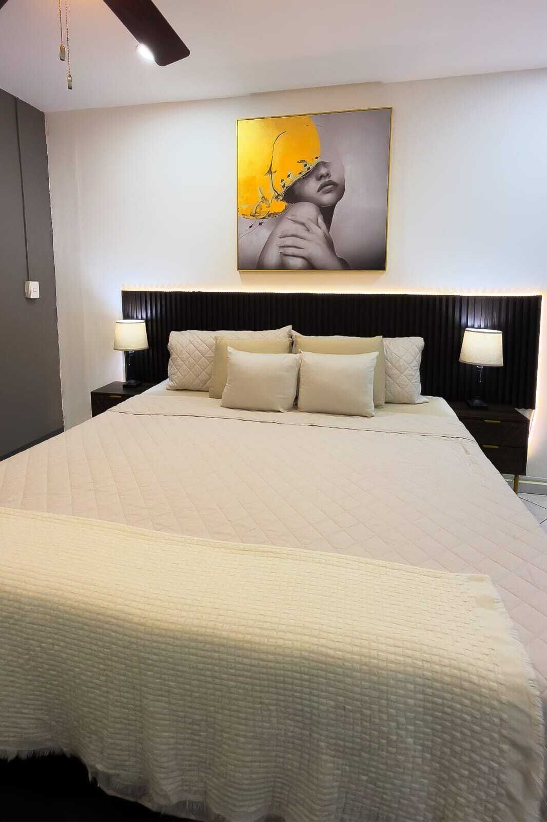 A hotel room with a large bed, two bedside tables, a ceiling fan, and a wall-mounted artwork.