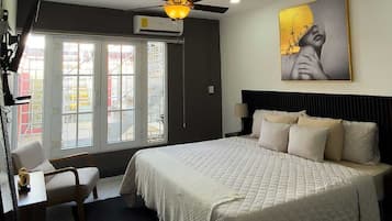 Une chambre d’hôtel équipée d’un lit, d’un bureau, d’une chaise, d’un ventilateur de plafond et d’une grande fenêtre.
