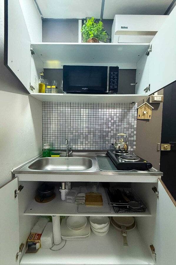 A compact kitchen with a microwave, sink, and kettle.