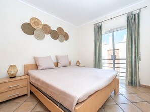 A modern bedroom with a large bed, a nightstand with a lamp, and a wall-mounted decorative item. - Quinta Gomeira - Top Floor 2 Bedroom with pool (Cabanas de Tavira)