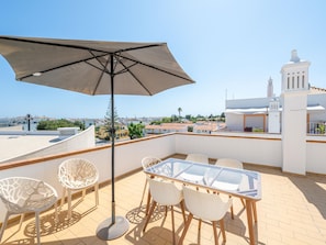 A rooftop terrace with a table and chairs, an umbrella, and a view of the cityscape. - Quinta Gomeira - Top Floor 2 Bedroom with pool (Cabanas de Tavira)
