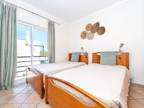 A room with two wooden beds, a sliding glass door, and a view of the outside. - Quinta Gomeira - Top Floor 2 Bedroom with pool (Cabanas de Tavira)