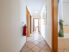 Ein Flur mit Fliesenboden, Holztüren, einem Feuerlöscher und einem Badezimmer mit Duschvorhang.