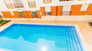 Ein rechteckiger, überdachter Pool mit Fliesenrand, umgeben von einer gefliesten Liegefläche.