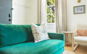 A teal sofa with a decorative pillow, a small wooden side table, and a framed picture on the wall.