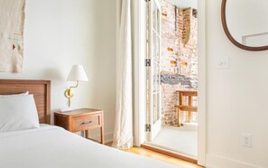 A hotel room with a bed, bedside table, lamp, and a view of an outdoor brick wall through a glass door. - Park House Parlor Level - 2 Bedroom/2 Bath Overlooking Monterey Square (Savannah)