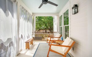 A covered porch with a ceiling fan, wooden chairs, a bench, and a view of greenery through the windows. - Park House Parlor Level - 2 Bedroom/2 Bath Overlooking Monterey Square (Savannah)