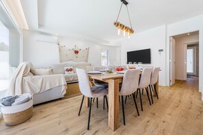 Een moderne woonkamer met een eethoek, met een houten eettafel, comfortabele zithoek, een grote flatscreen televisie en een gezellige open haard.