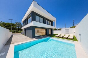 Ein modernes, zweistöckiges Haus mit Swimmingpool und Gartenmöbeln.