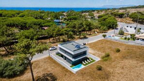 Ein modernes, zweistöckiges Gebäude mit Pool auf dem Dach und Solaranlage, umgeben von einer natürlichen Landschaft und freiem Blick auf das Meer.