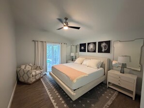 Quarto com cama, mesas de cabeceira, ventoinha no teto e obra de arte na parede.