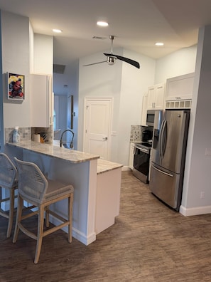 A modern kitchen with a central island, two chairs, a refrigerator, and a ceiling fan. - Welcome to our beautiful 3-bedroom, 2-bath home in the heart of Marco Island! (Marco Island)