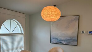 A dining area with a round table, four chairs, a hanging light fixture, a window with blinds, and a painting on the wall. - Welcome to our beautiful 3-bedroom, 2-bath home in the heart of Marco Island! (Marco Island)