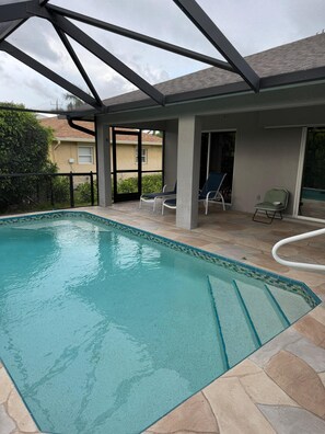 Piscina coberta com espreguiçadeiras e vista para o quintal.