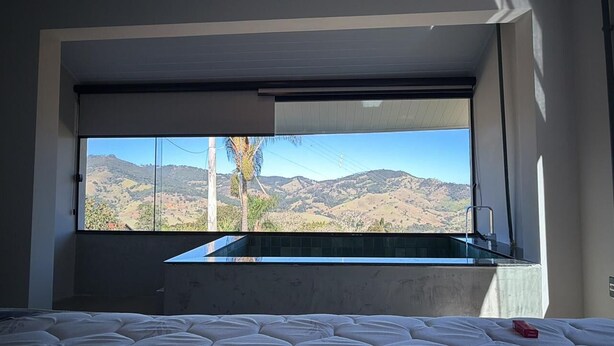 A bedroom with a large window, a bed, and a view of a mountainous landscape.