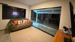 A living room with a sofa, a flat-screen TV, a wooden coffee table, and a large glass door leading to an outdoor area.