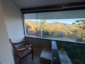 A balcony with a wooden chair, a tiled floor, and a view of a hilly landscape. - Deusmideu Refuge (São Bento do Sapucaí)